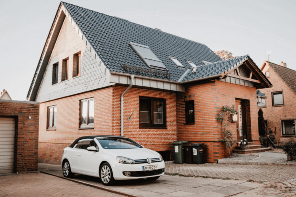 Een witte auto staat geparkeerd voor een huis op de oprit.